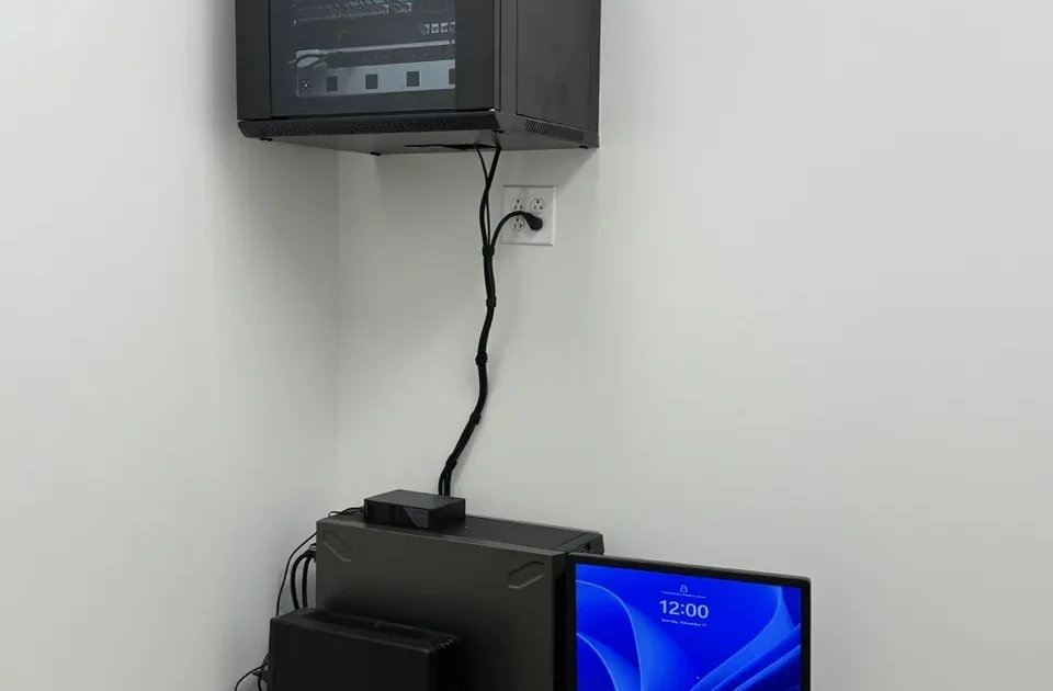 Network cabling setup with a wall-mounted server and a desktop monitor displaying time, illustrating IT infrastructure for business operations.